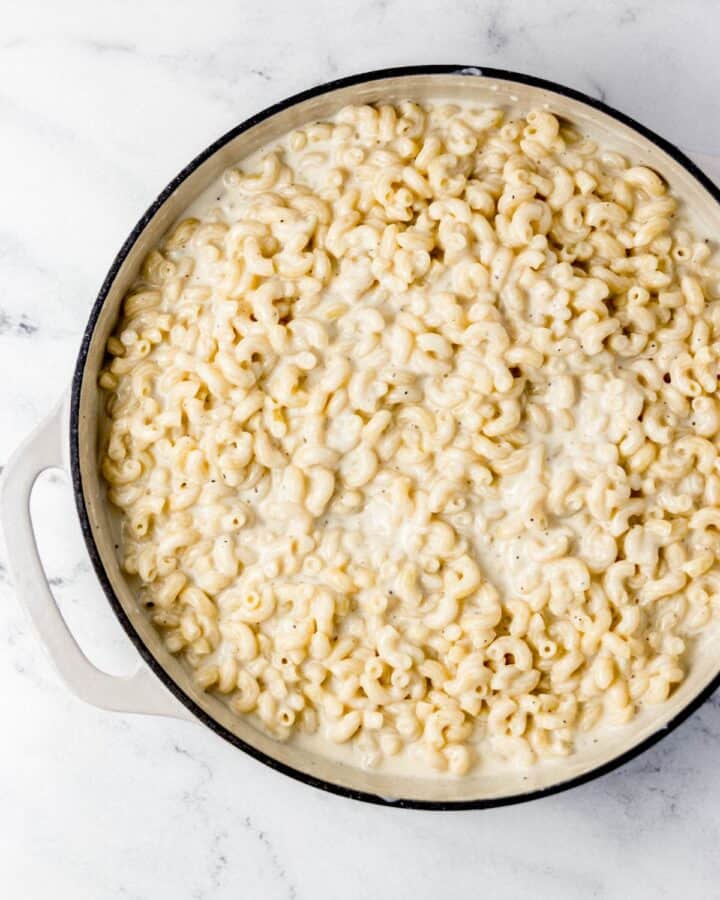 Overhead view of mac and cheese ingredients combined in large white braiser pan. 