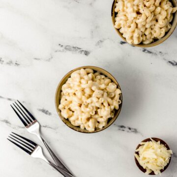 Overhead view of finished mac in two bowls by small bowl of cheese and forks.