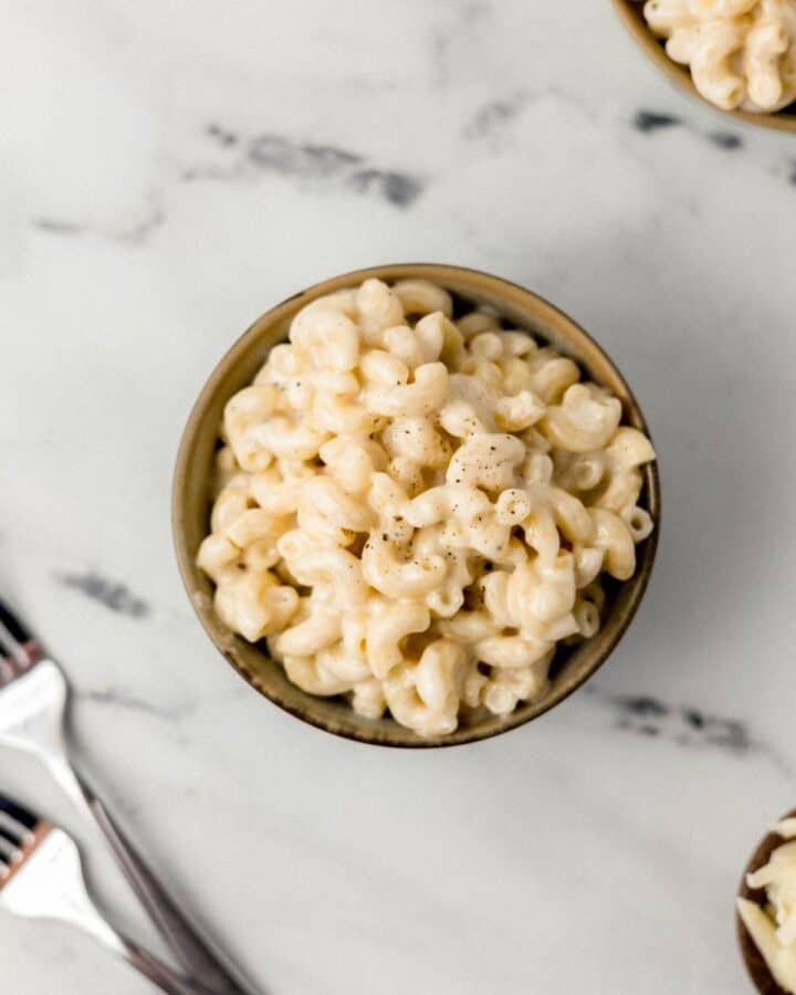 Overhead view of bowl of finished mac and cheese by forks on marble surface.