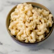 Close up front view of serving of mac and cheese in grey bowl topped with black pepper.