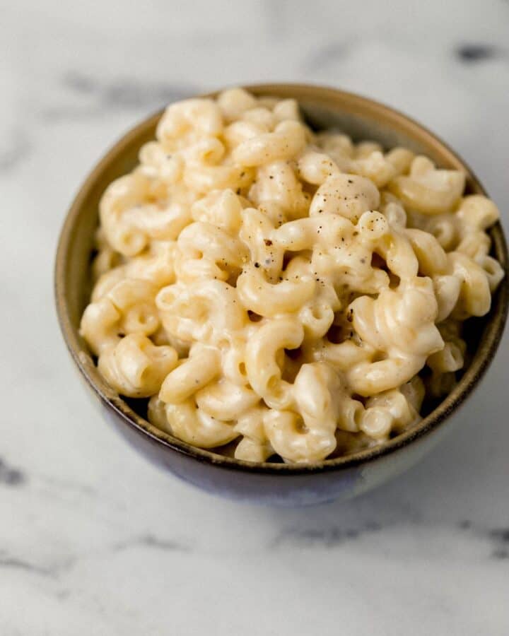 Close up view of finished pasta in small bowl on marble surface. 