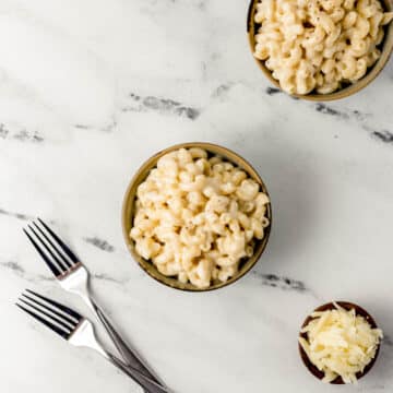 white cheddar mac and cheese in two small bowls with small bowl of shredded cheese and two forks