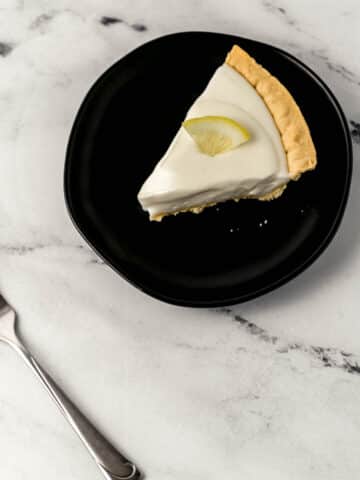 slice of lemonade pie on black plate beside a fork on marble surface