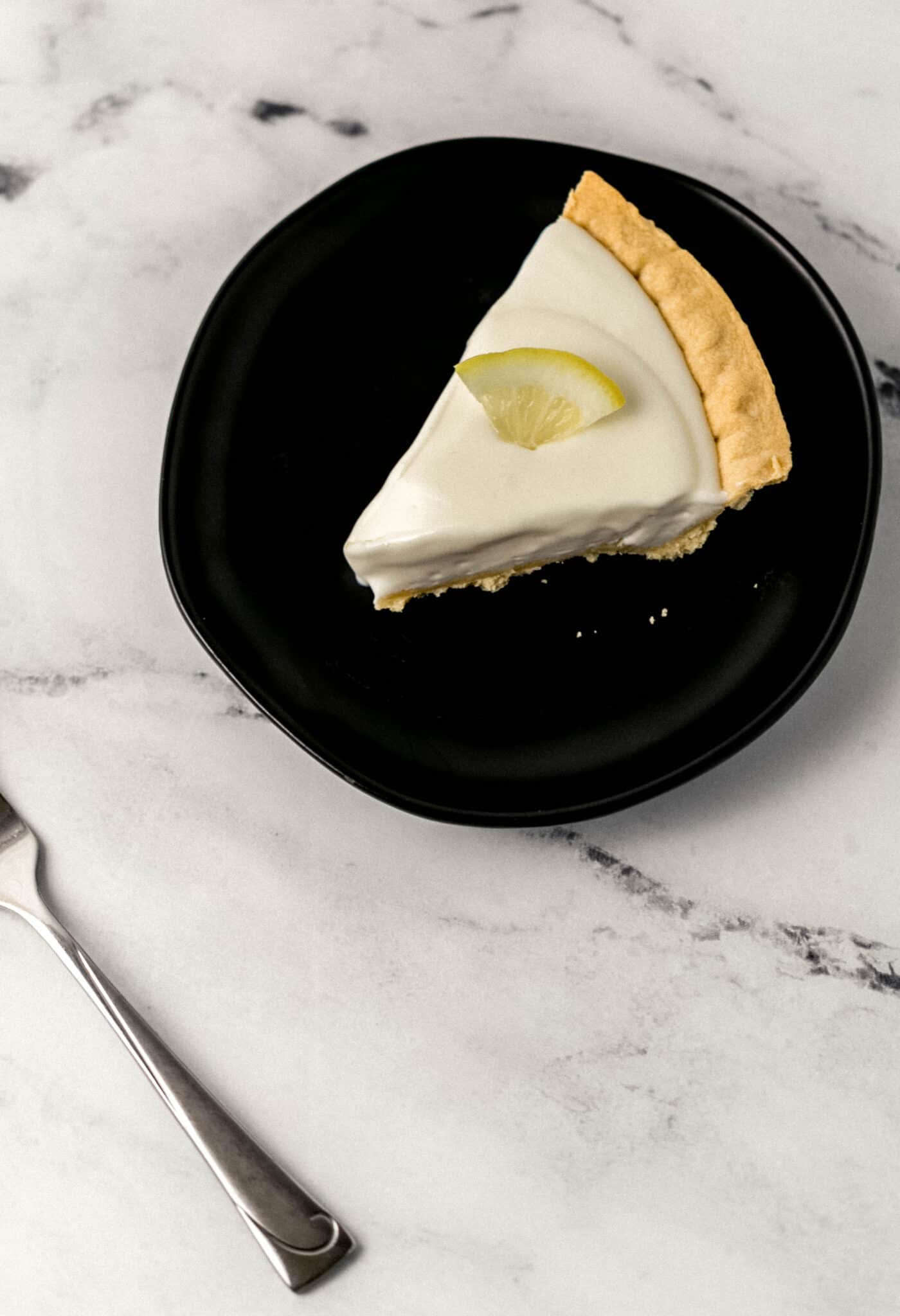 slice of lemonade pie on black plate next to a fork