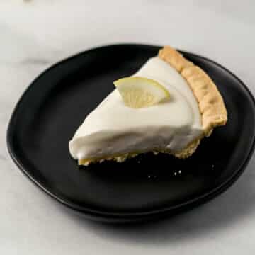 slice on lemonade pie on black plate topped with lemon