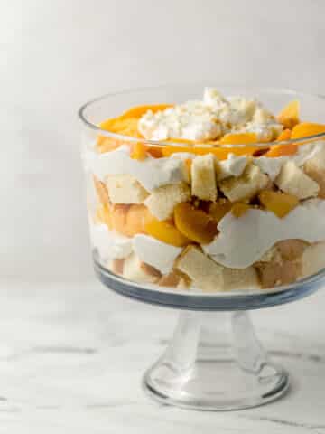 close up side view of finished peach trifle topped with cream
