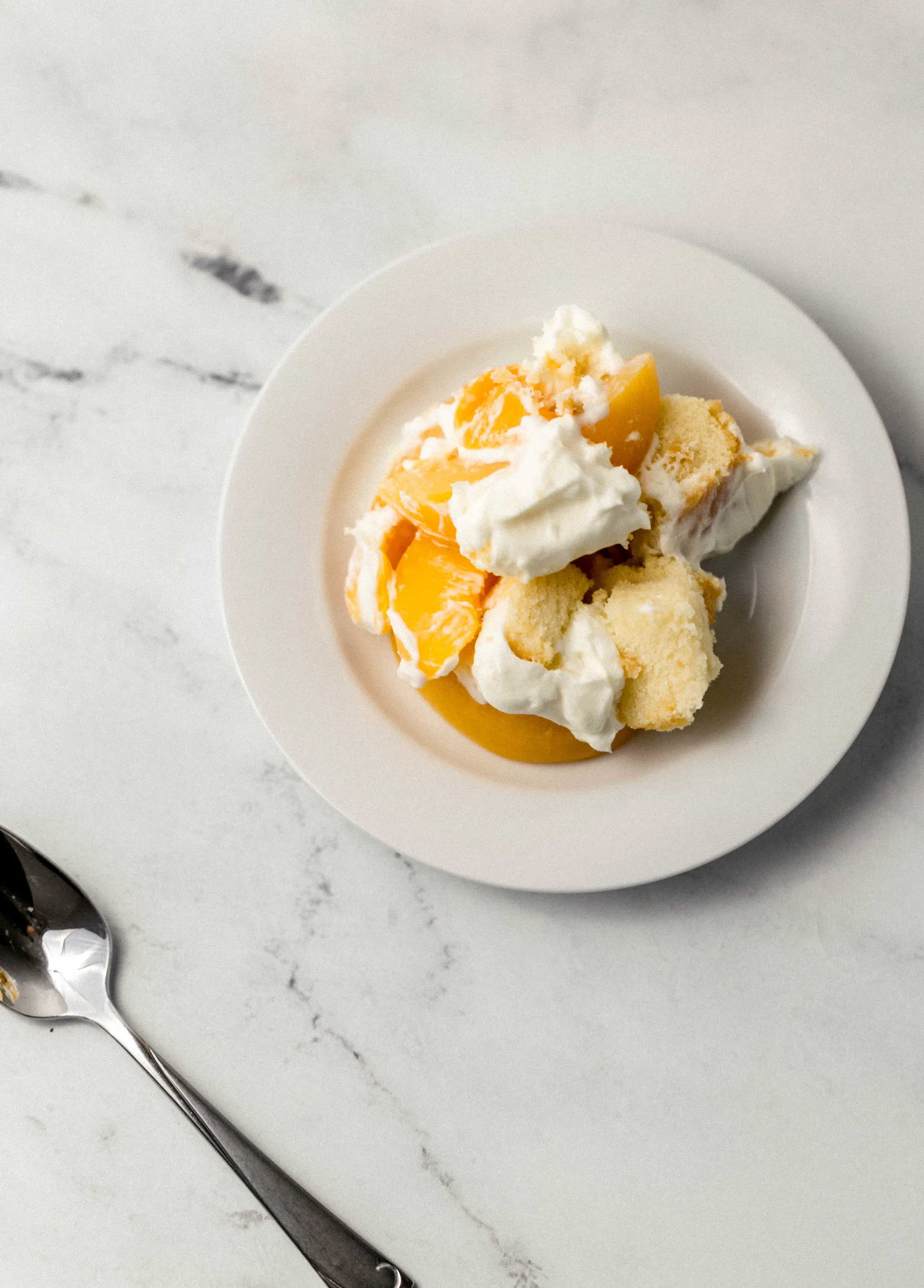 small white plate of serving of peach trifle with a spoon