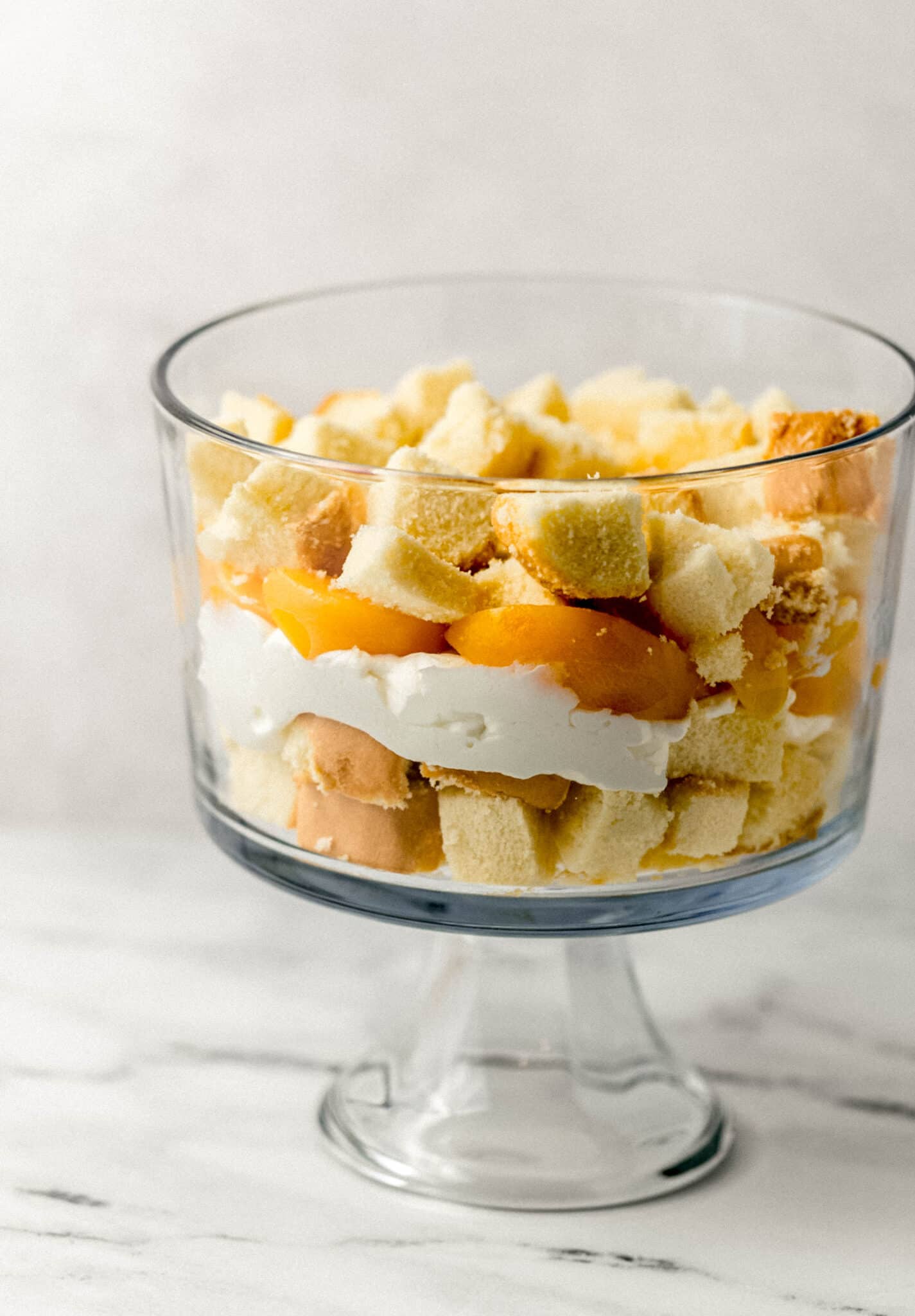 close up side view of peach trifle in process of being assembled