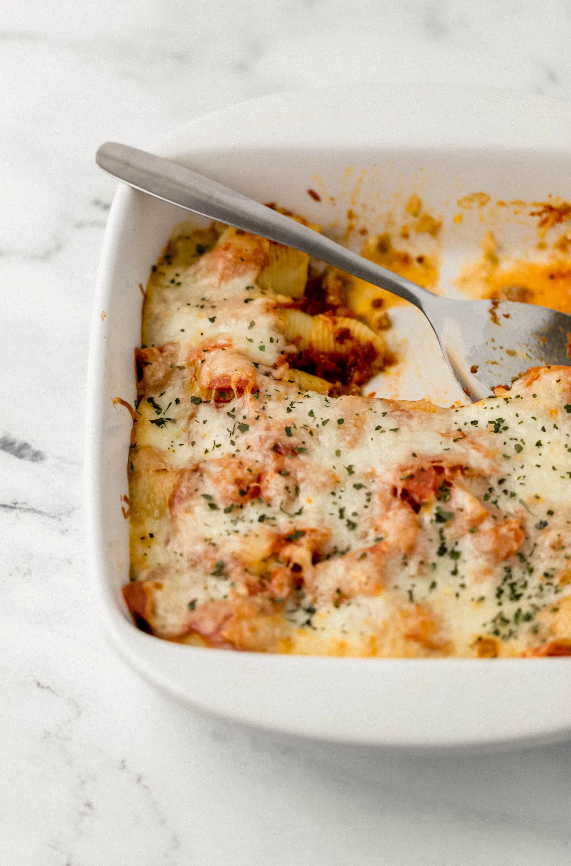 close up side view of stuffed shells in white baking dish with serving spoon