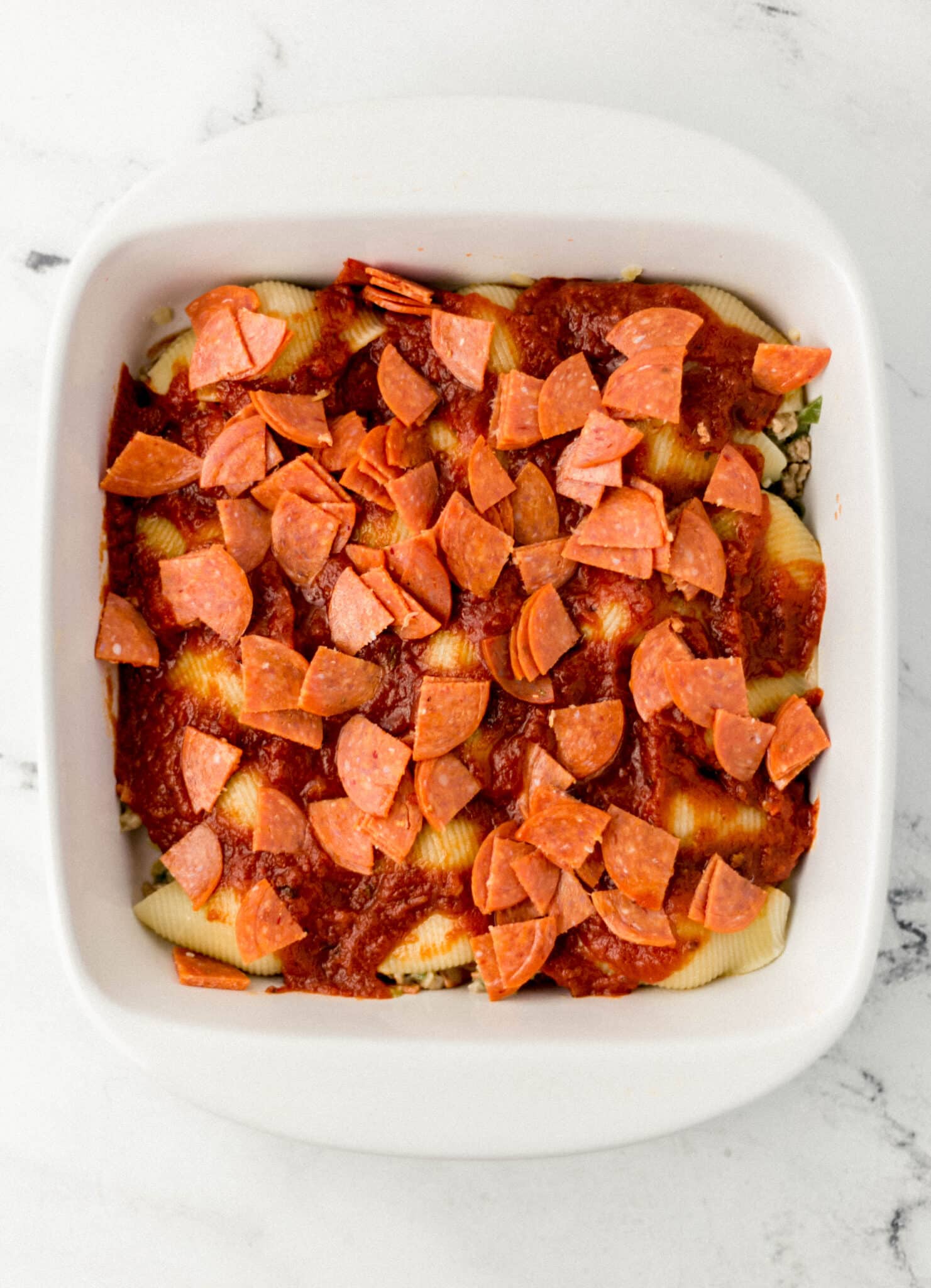 pasta shells covered with pasta sauce and pepperoni in baking dish 