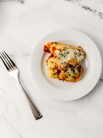 overhead view of white plate with supreme pizza pasta shells on it beside a fork on marble surface