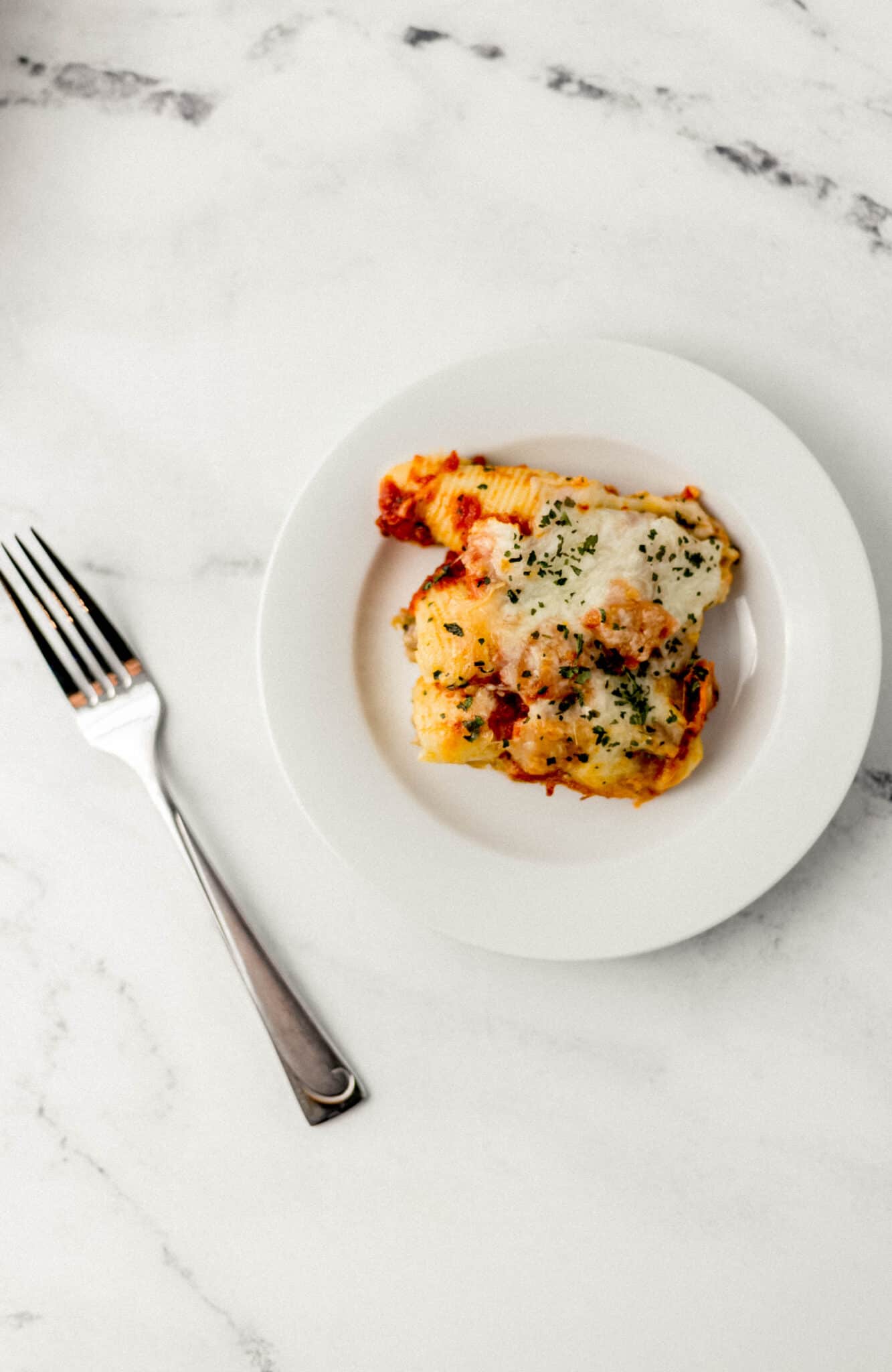 overhead view of white plate with supreme pizza stuffed shells on it beside a fork on marble surface.