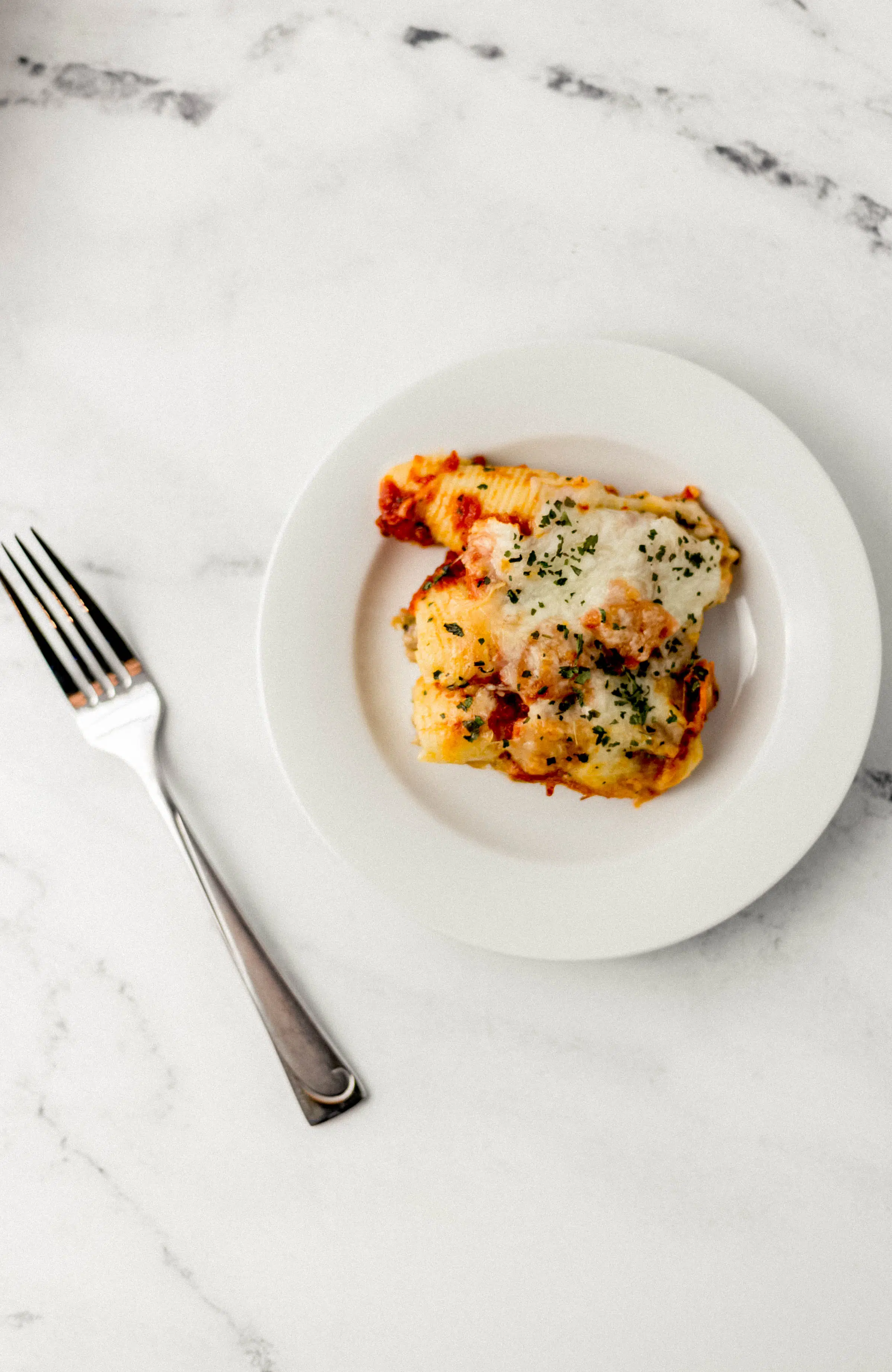 Pizza Stuffed Shells Simply LaKita 5 overhead view of white plate with supreme pizza stuffed shells on it beside a fork on marble surface.
