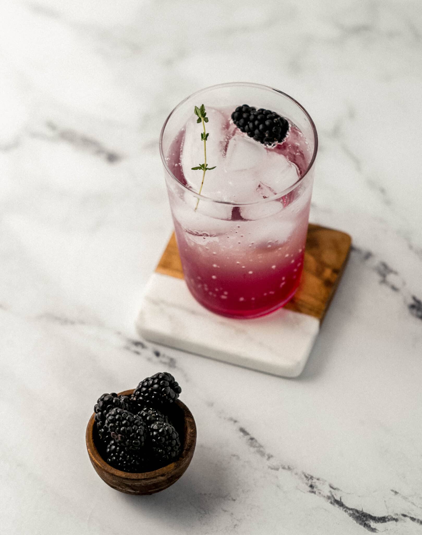 finished mocktail in glass on coaster with small bowl of blackberries.