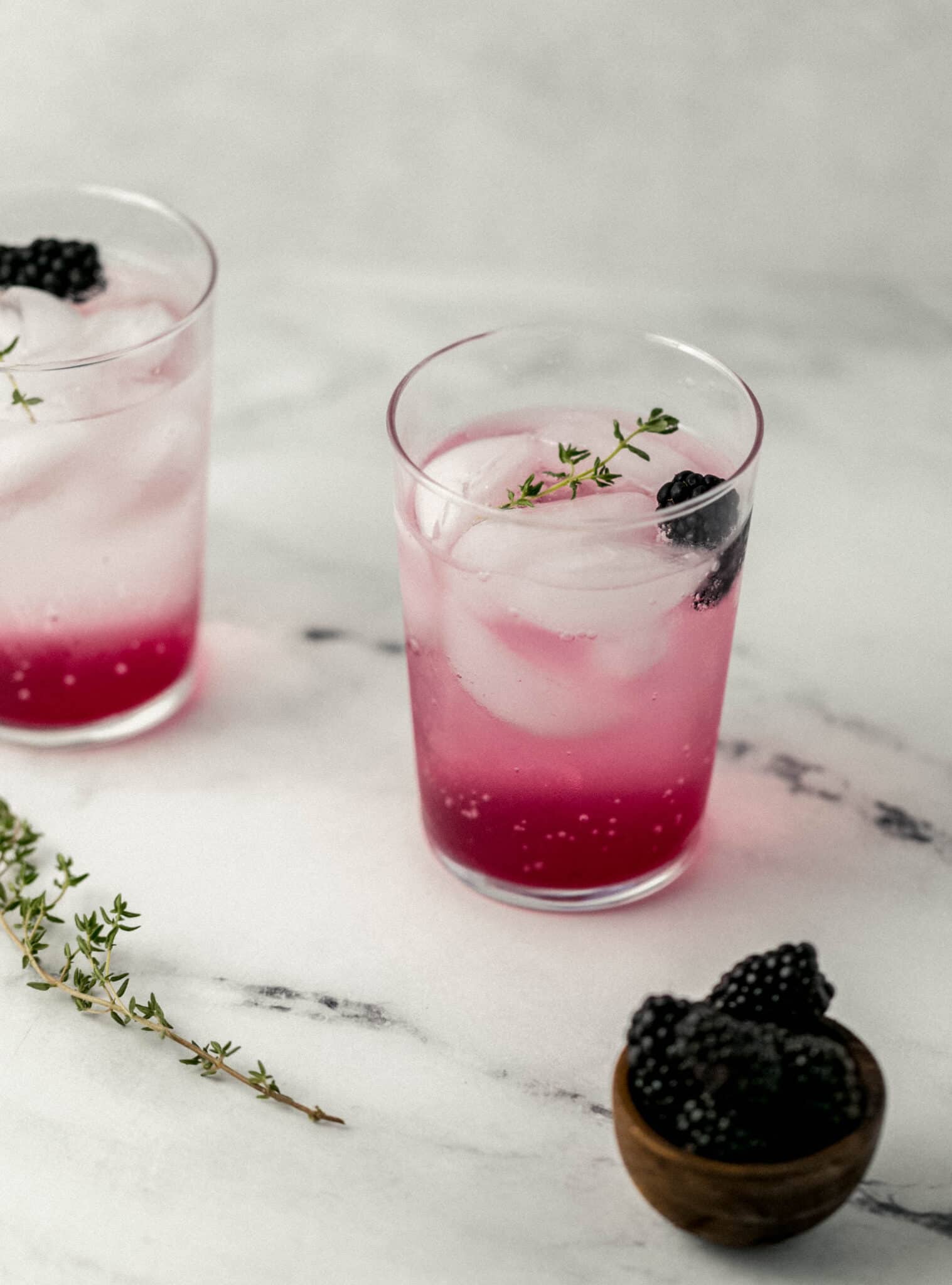 close up side view two glasses with blackberry thyme mocktail in them. 