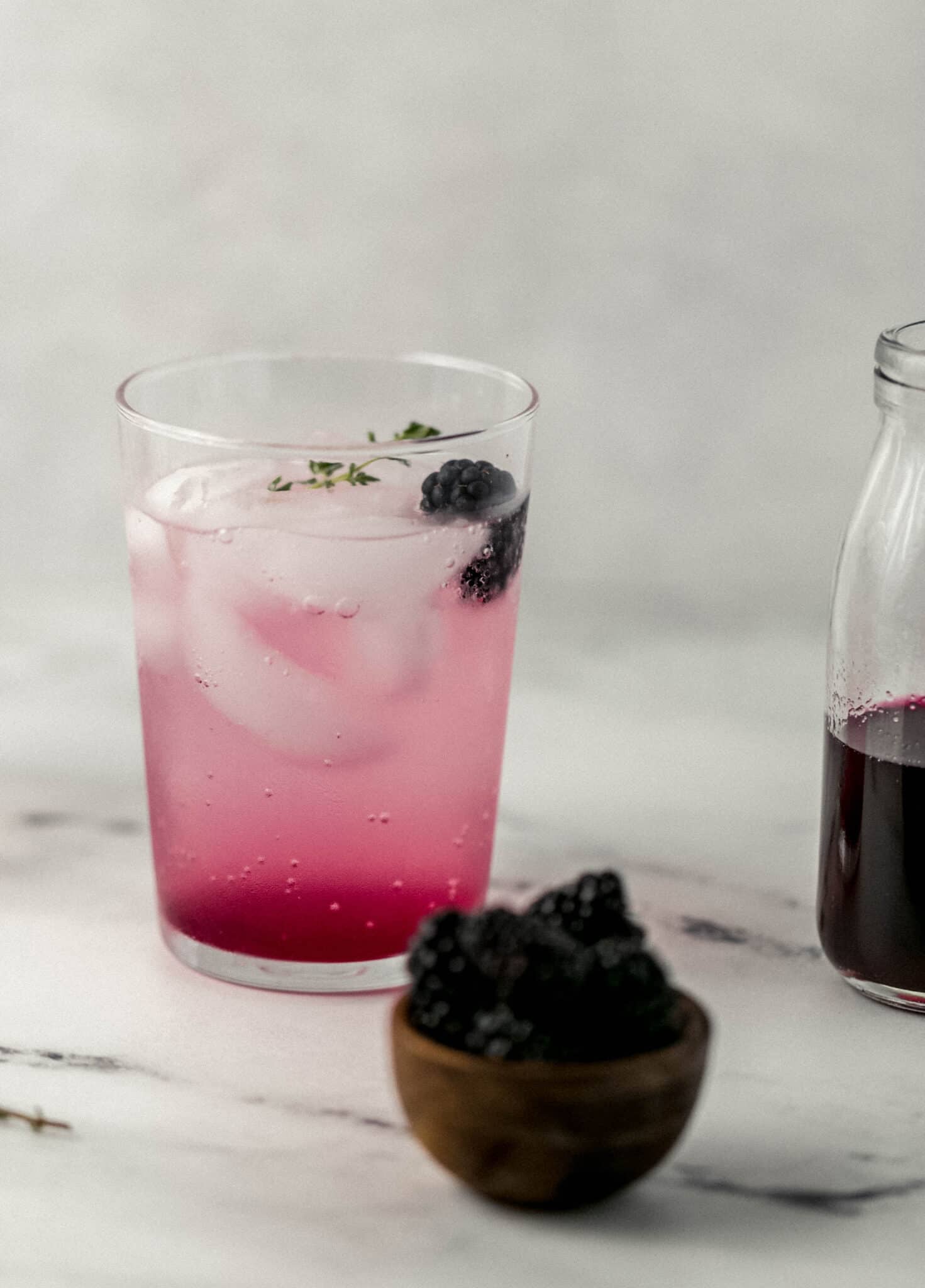 close up side view of drink next to bowl with blackberries in it. 