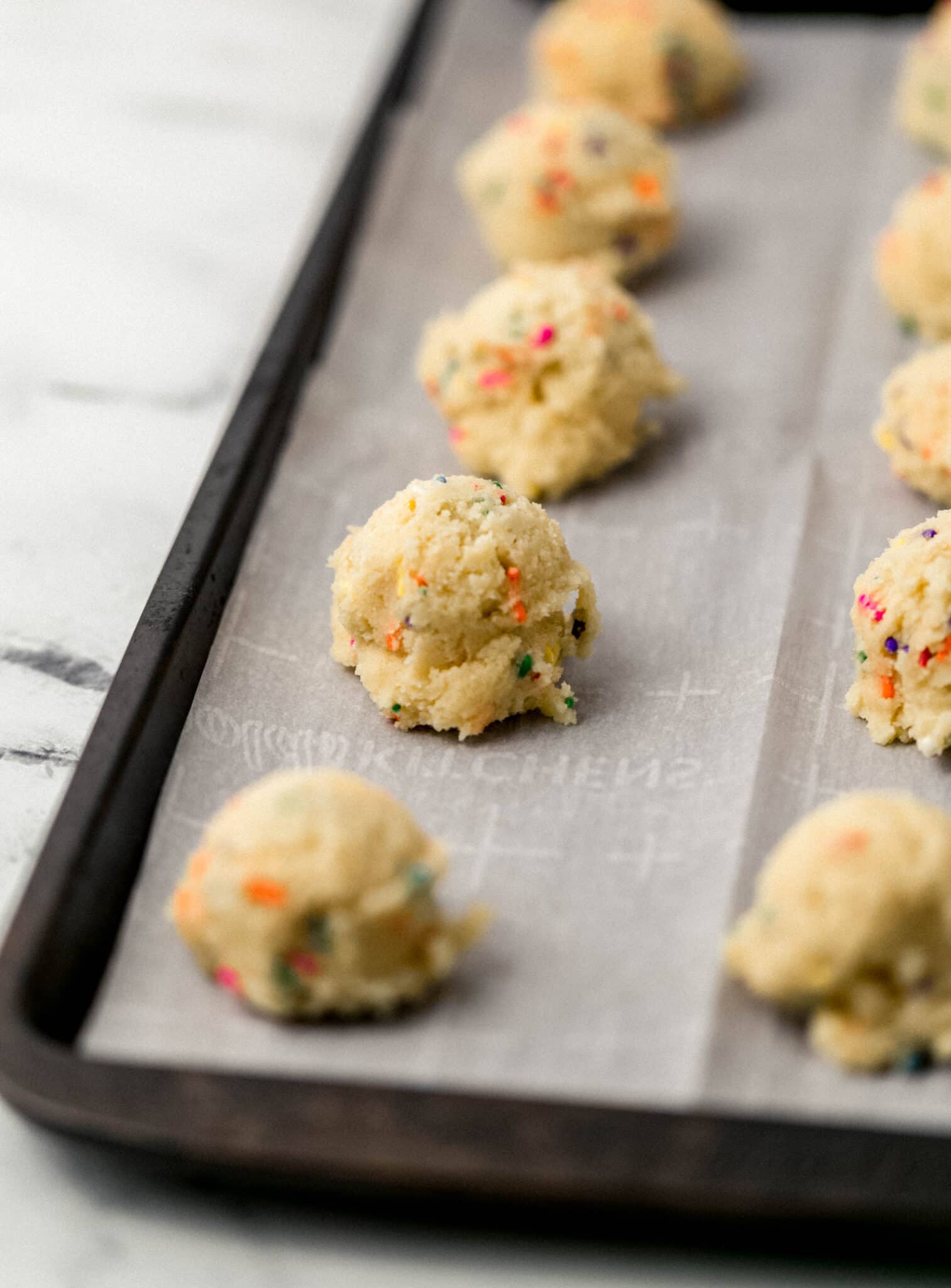 close up side view cookie dough on parchment-lined baking sheet 