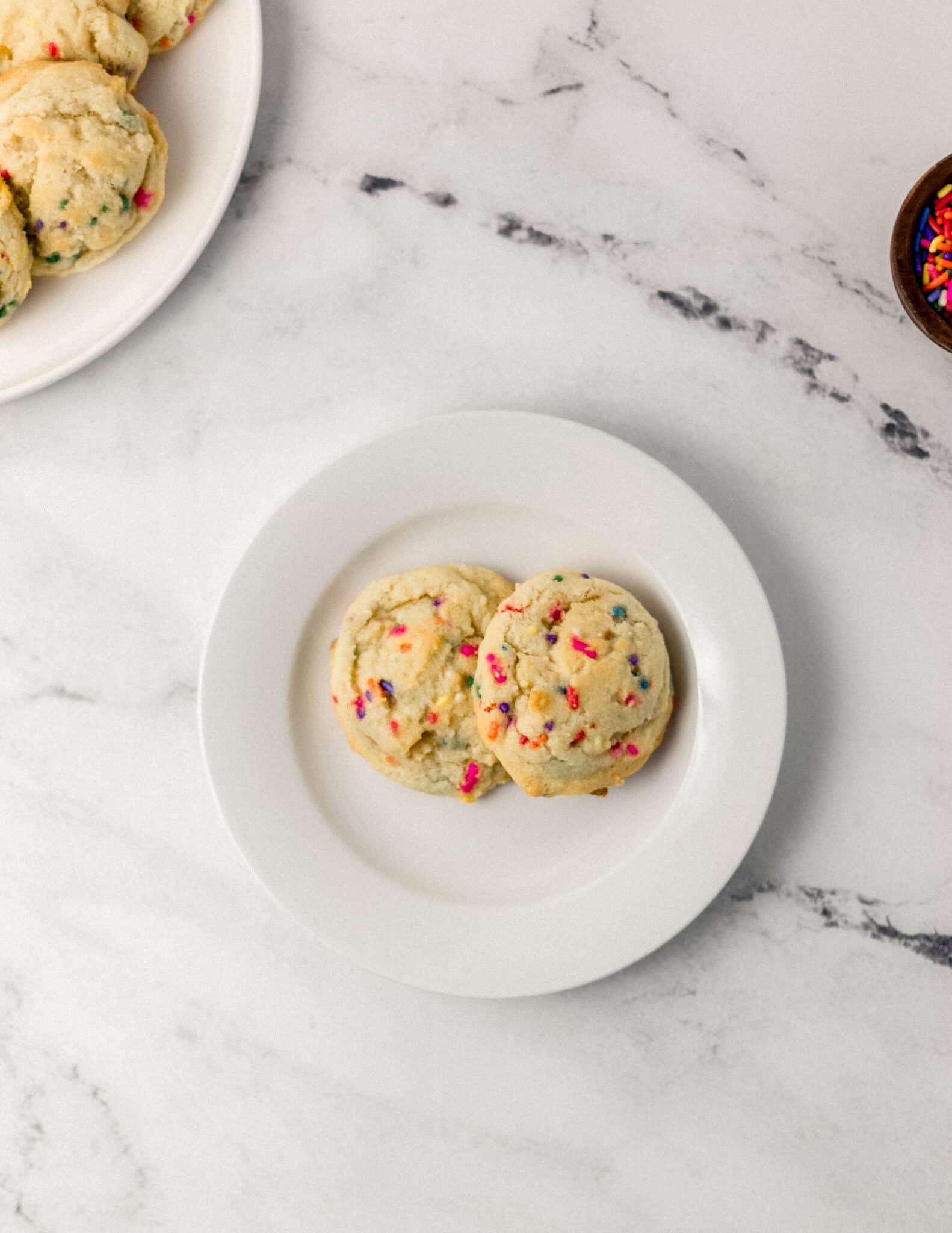 white plate with two finished funfetti sugar cookies on it