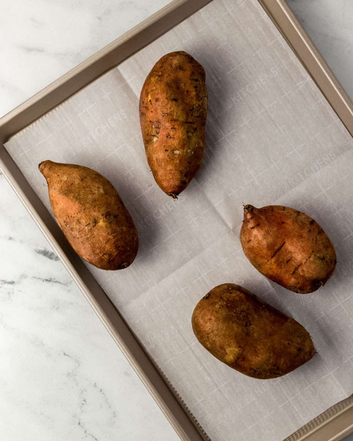 Overhead view of whole sweet potatoes on parchment lined sheet pan.