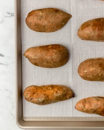 Sweet potatoes cut in half and placed on parchment lined sheet pan.
