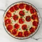 Overhead view of pepperoni dip in glass baking dish on marble surface.