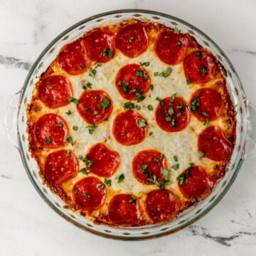 Overhead view of pepperoni dip in glass baking dish on marble surface.
