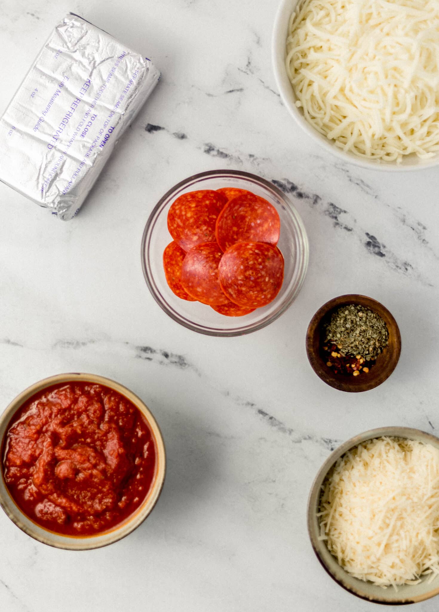 ingredients to make pepperoni pizza dip in separate containers on marble surface 