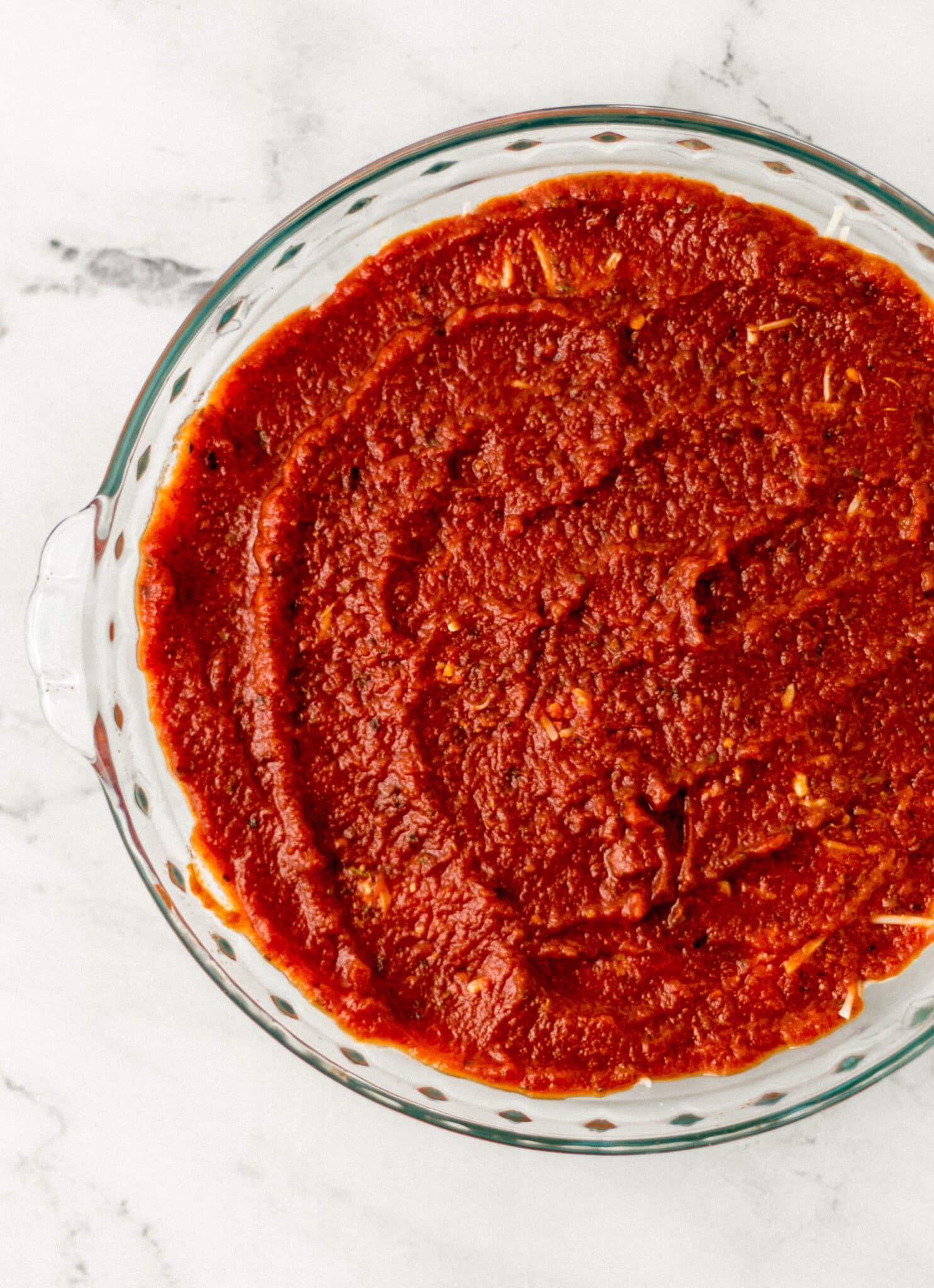 layer of pizza sauce spread over dip in glass dish 