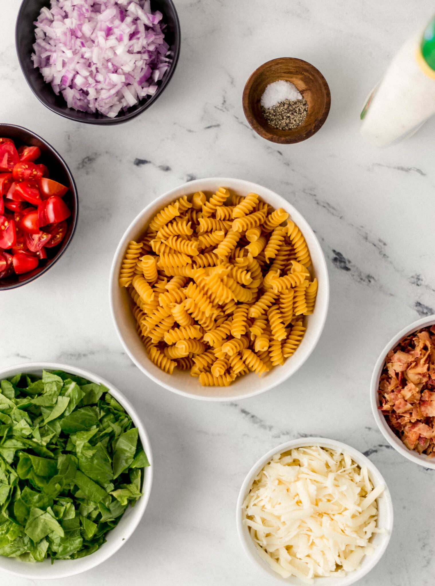 ingredients needed to make ranch blt pasta salad in separate bowls on marble surface 