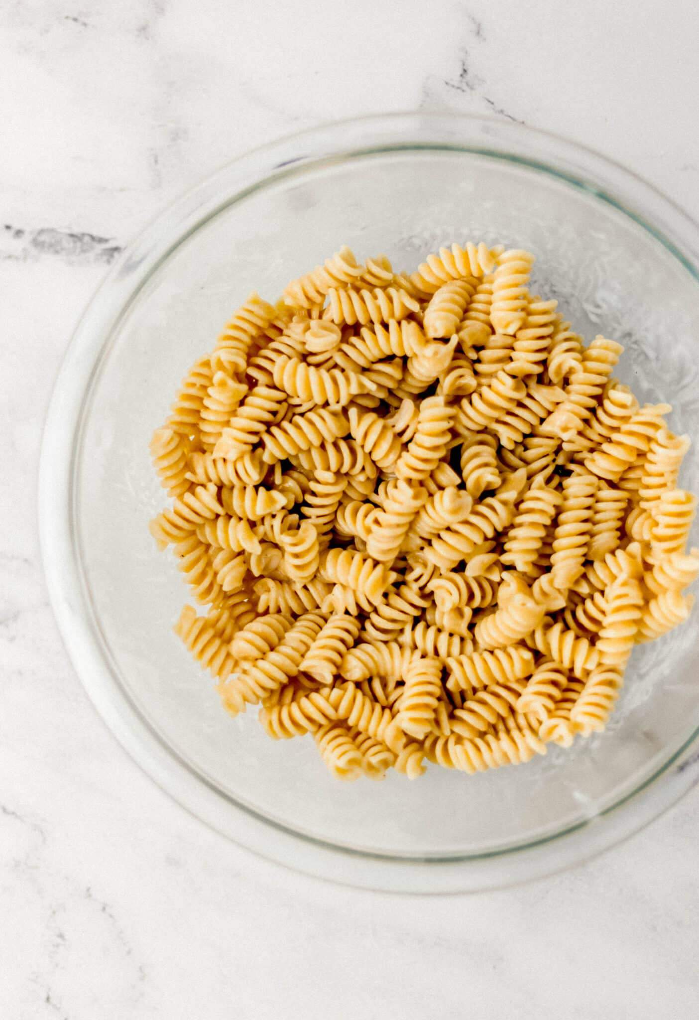 overhead view of pasta tossed in dressing in glass bowl 