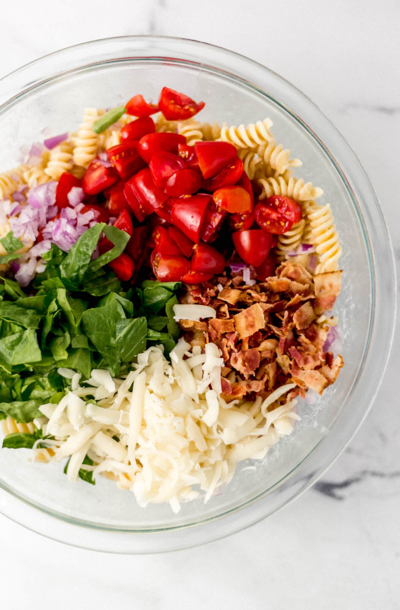 ingredients to make pasta salad combined in glass bowl 