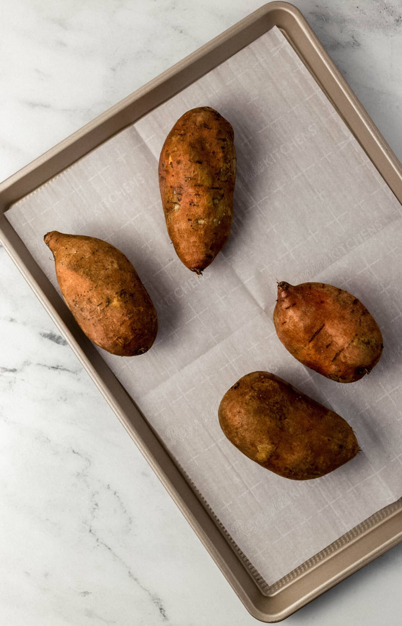 whole sweet potatoes on parchment-lined sheet pan 