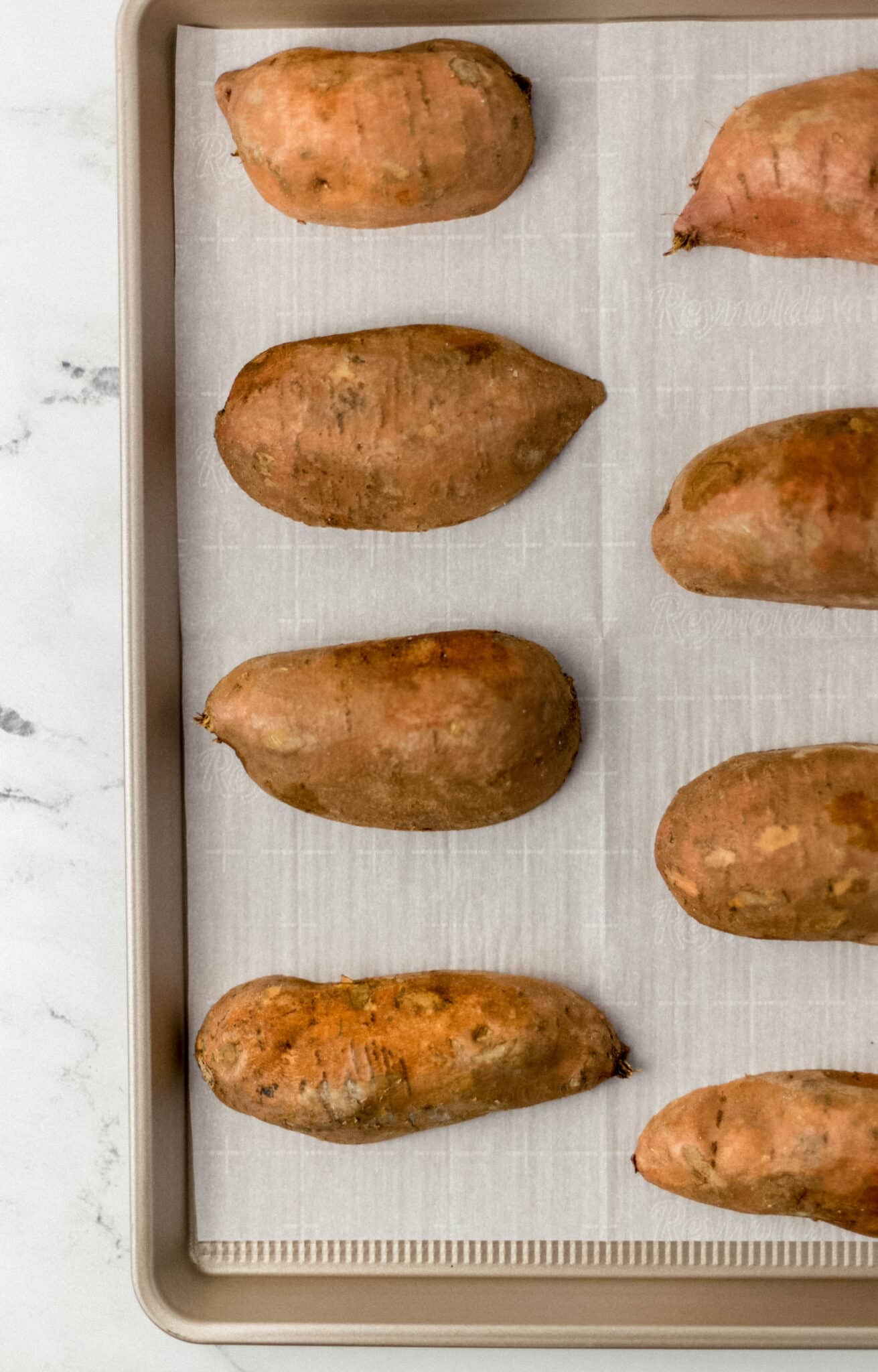 sheet pan lined with parchment-paper and raw sweet potatoes cut in half 