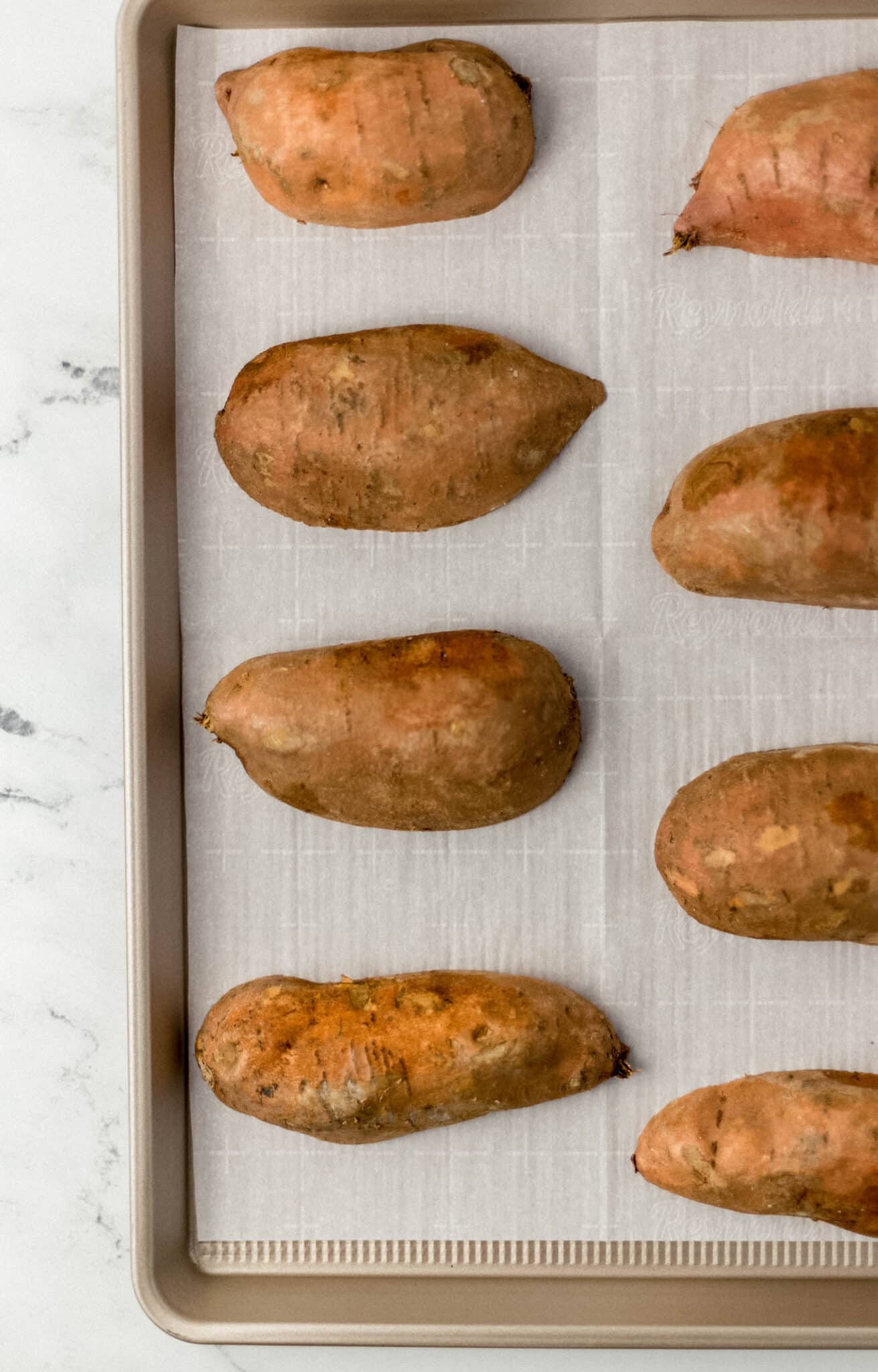 sheet pan lined with parchment-paper and raw sweet potatoes cut in half
