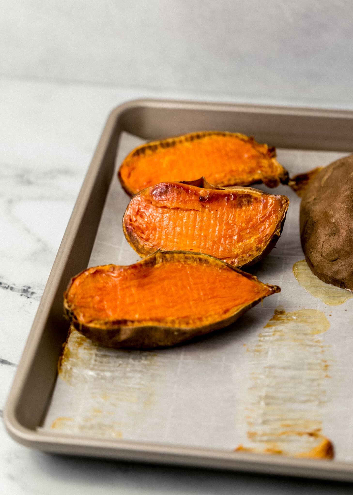 roasted sweet potatoes cut in half on parchment-lined sheet pan 