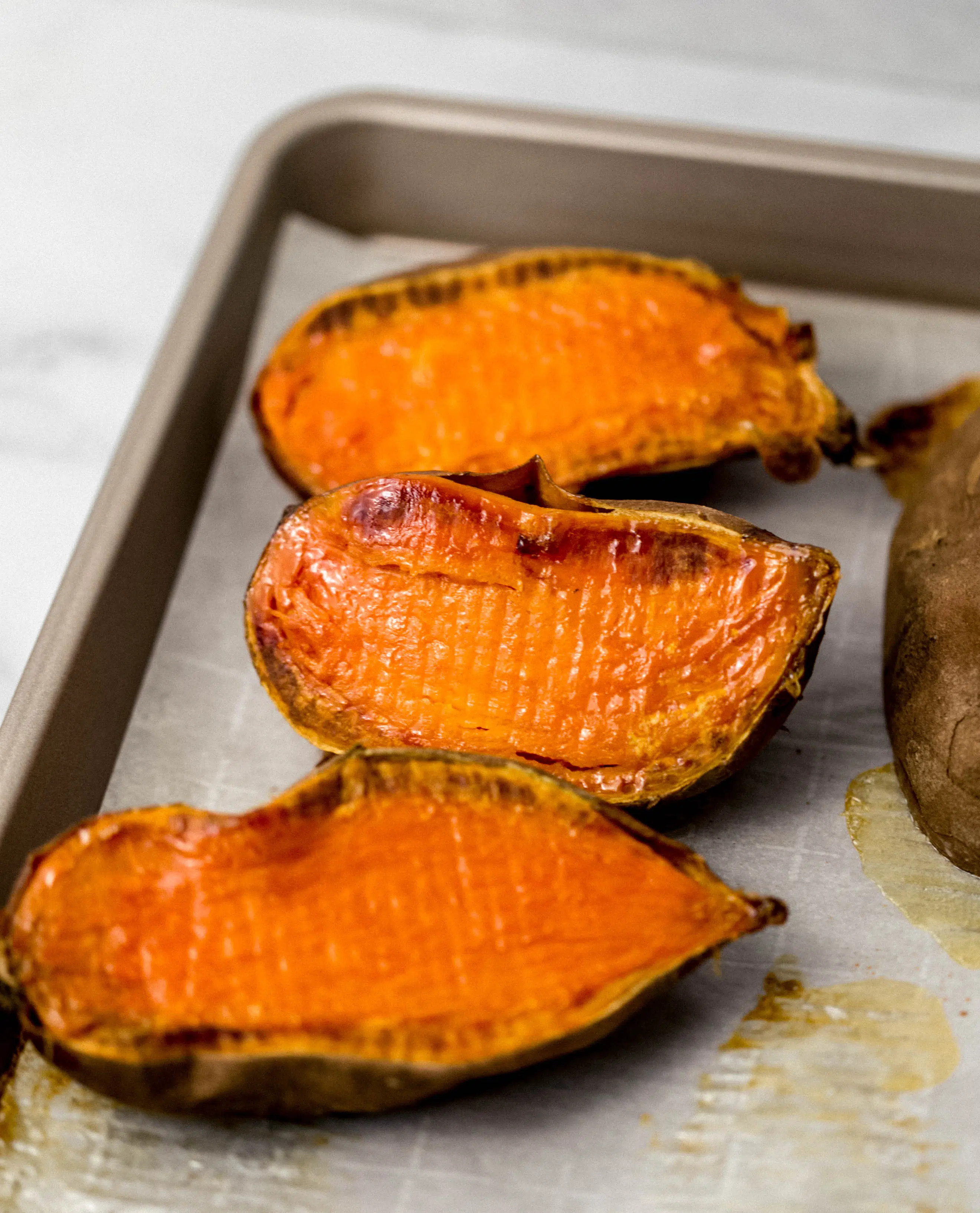cooked sweet potato halves on sheet pan