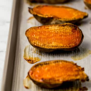 close up side view of finished roasted sweet potatoes on parchment-lined baking sheet