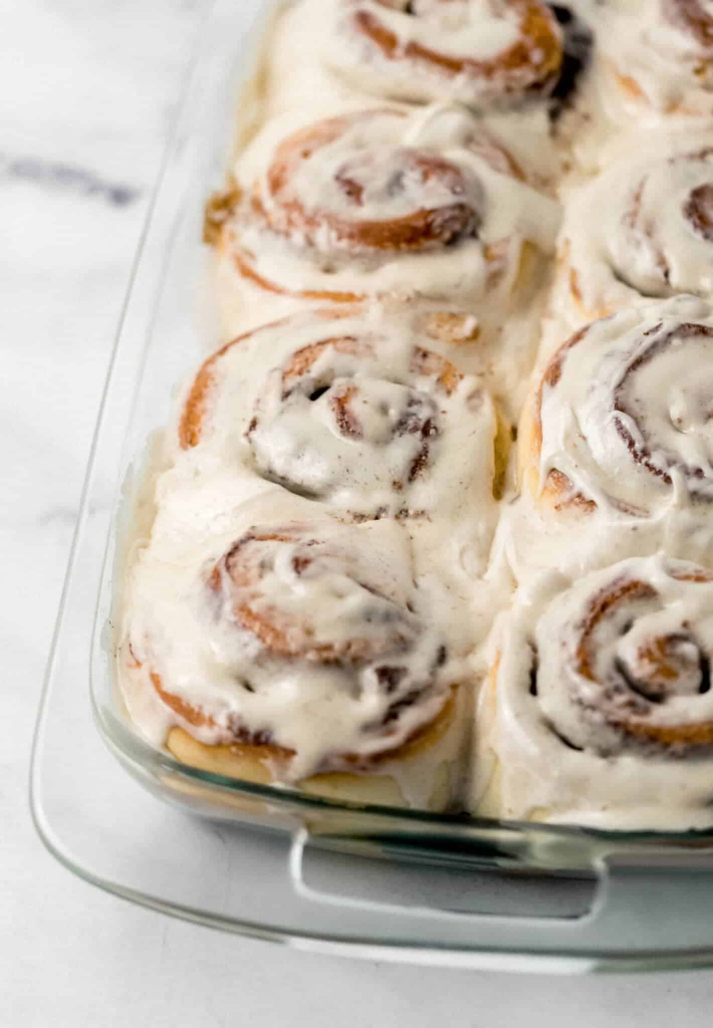 close up of finished cinnamon rolls topped with frosting in glass baking dish
