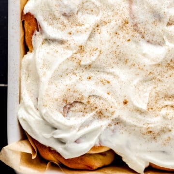 Close up overhead view of cinnamon rolls topped with icing in parchment lined baking dish.