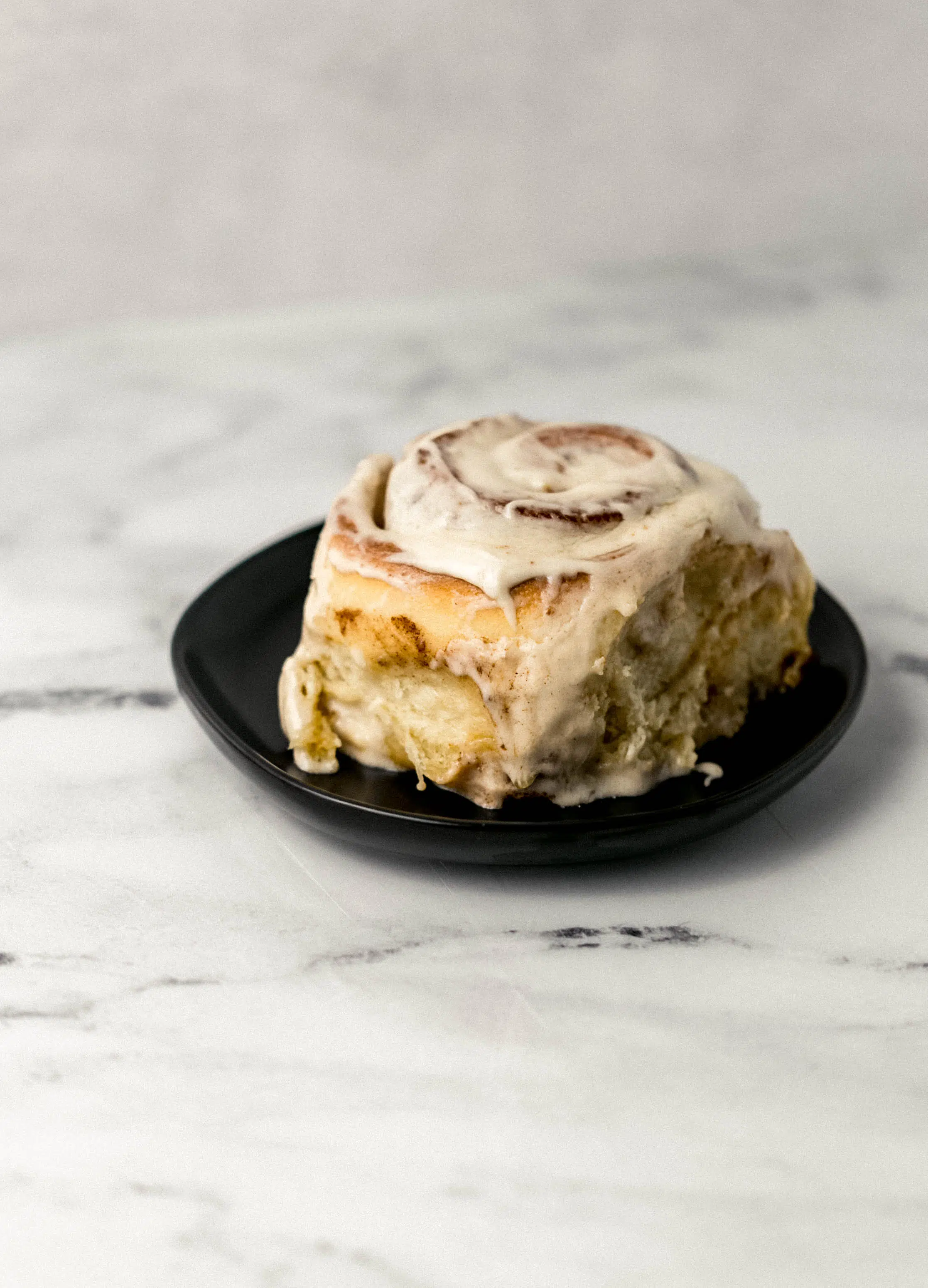 single cinnamon roll on small black plate. 