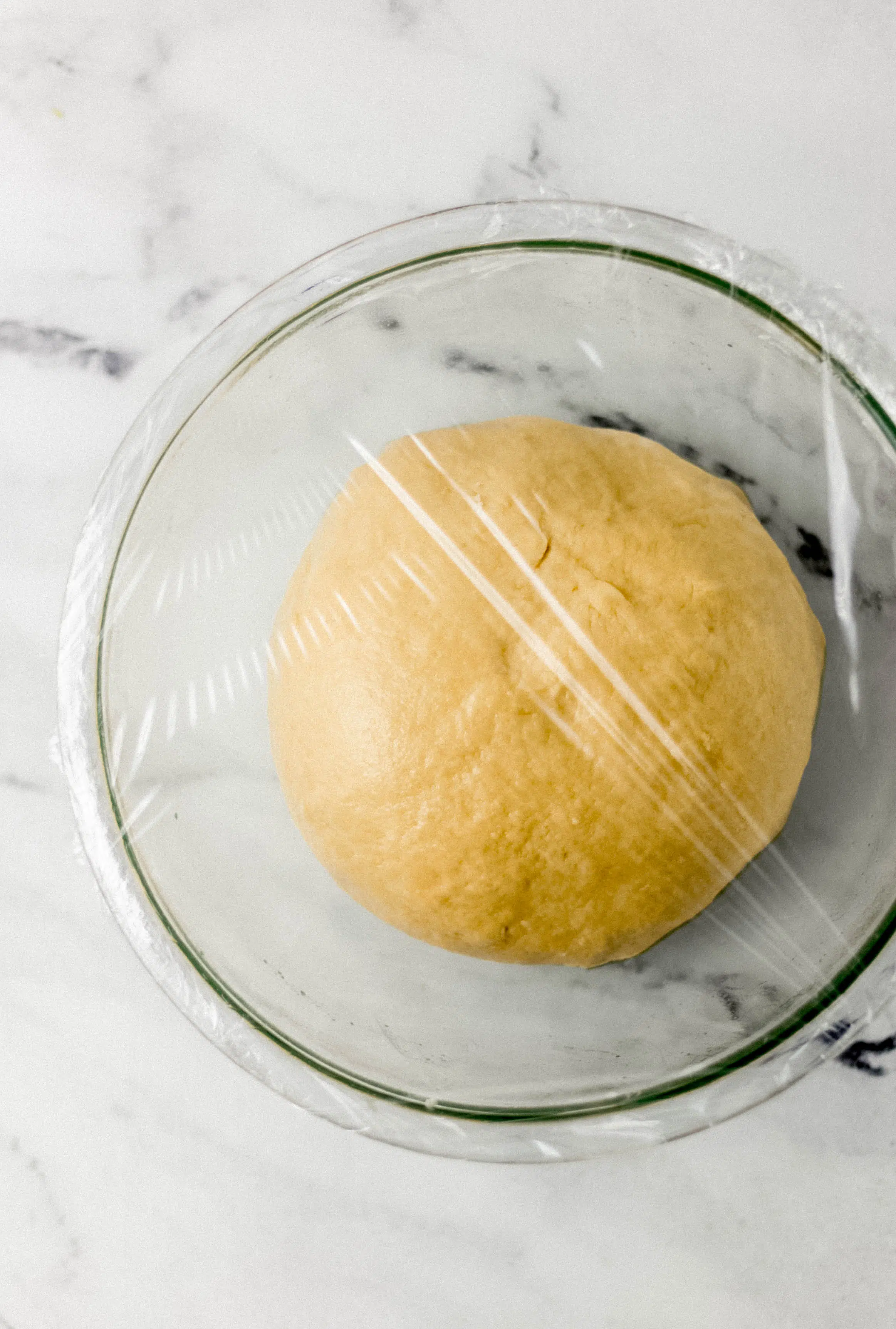 dough ball in glass mixing bowl covered with plastic wrap