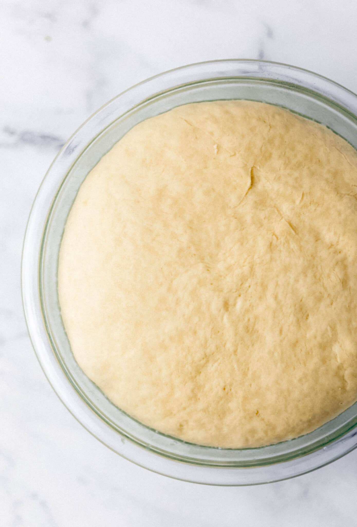 risen dough in glass mixing bowl