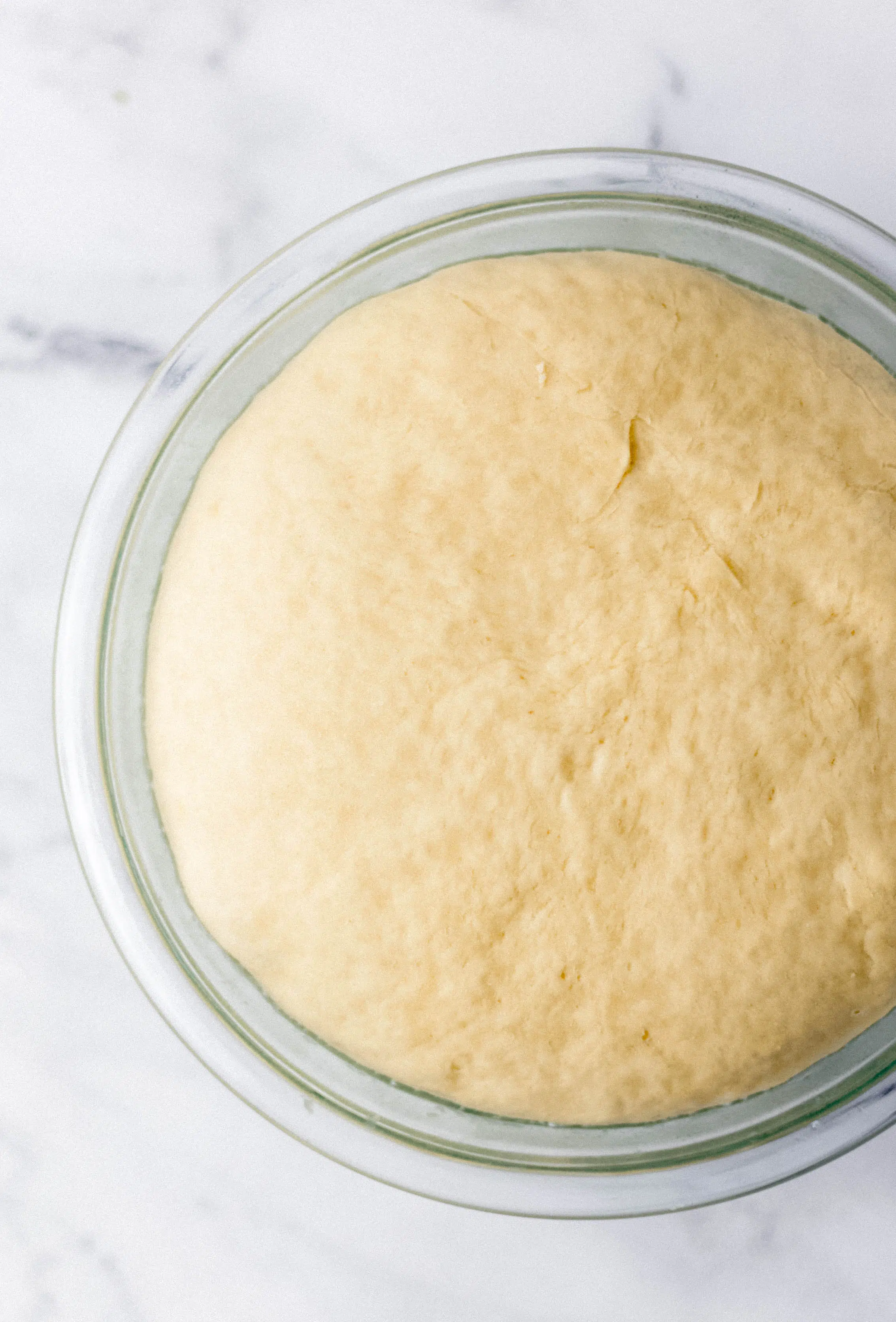 risen dough in glass mixing bowl