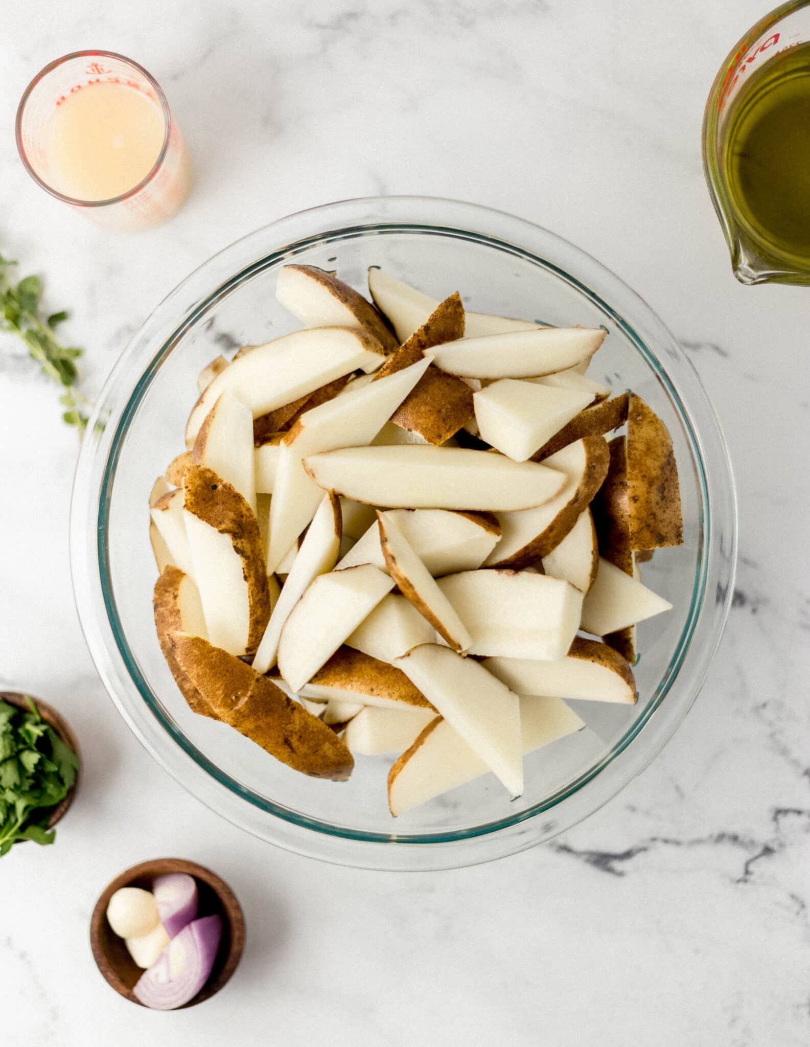 ingredients needed to make Greek potatoes on marble surface in separate containers