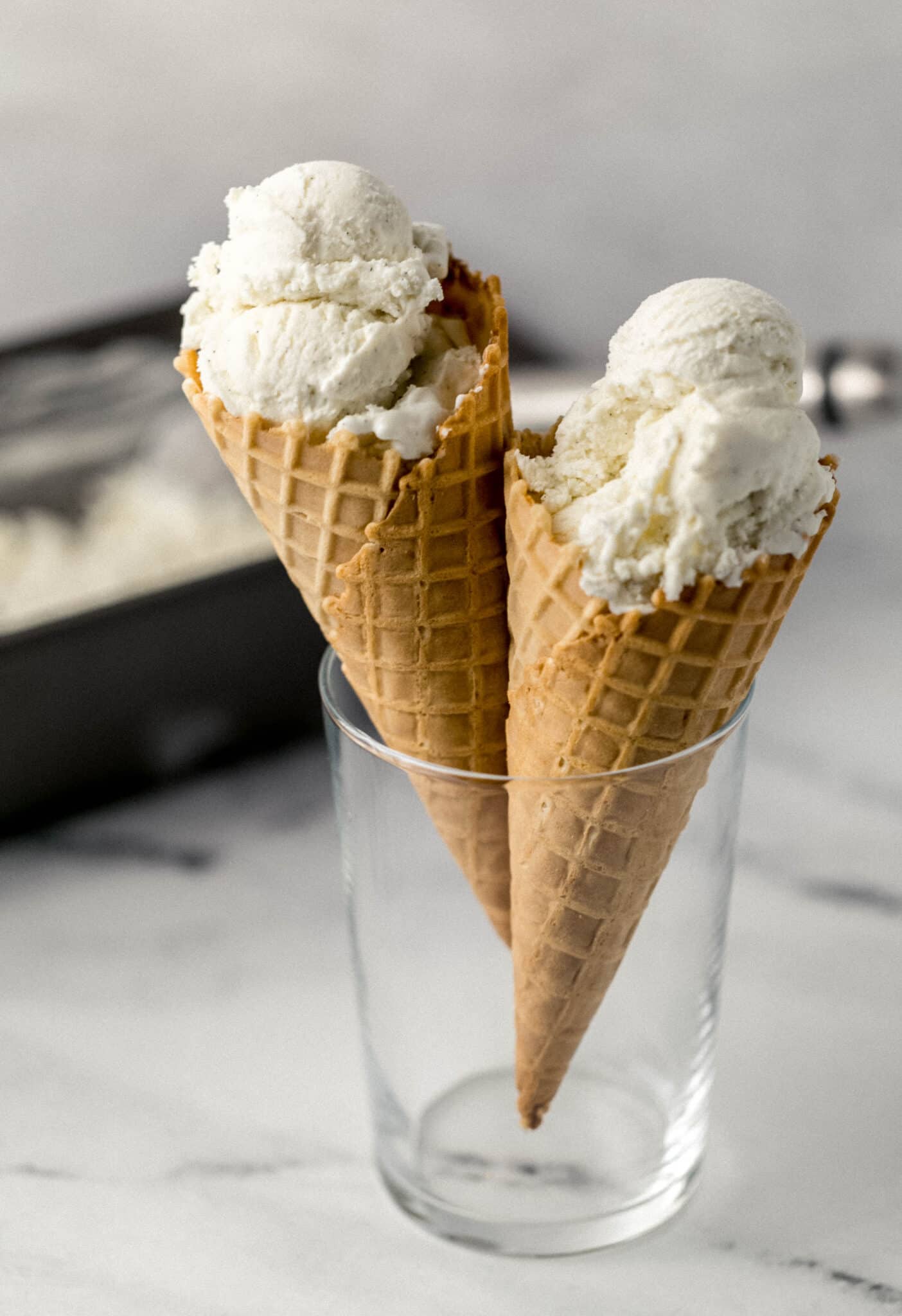 two vanilla ice cream cones in a glass with ice cream in the background