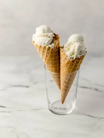 close up side view of two ice cream cones with vanilla ice cream in a glass