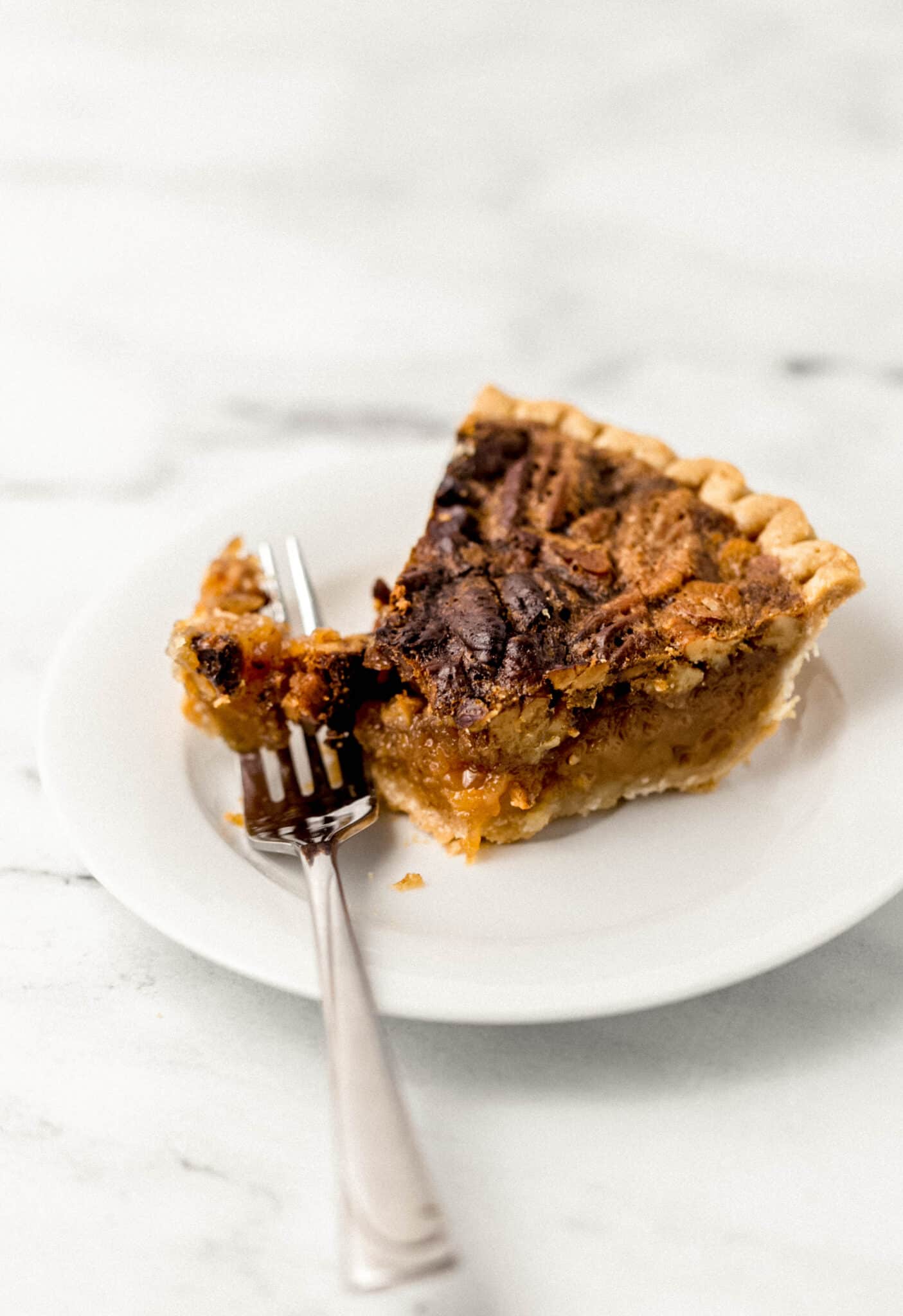 single slice of pecan pie on small white plate with a cutting into it