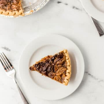 slice of pecan pie on white plate with whole pie and another slice with forks