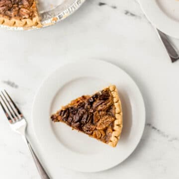 slice of pecan pie on white plate with whole pie and another slice with forks