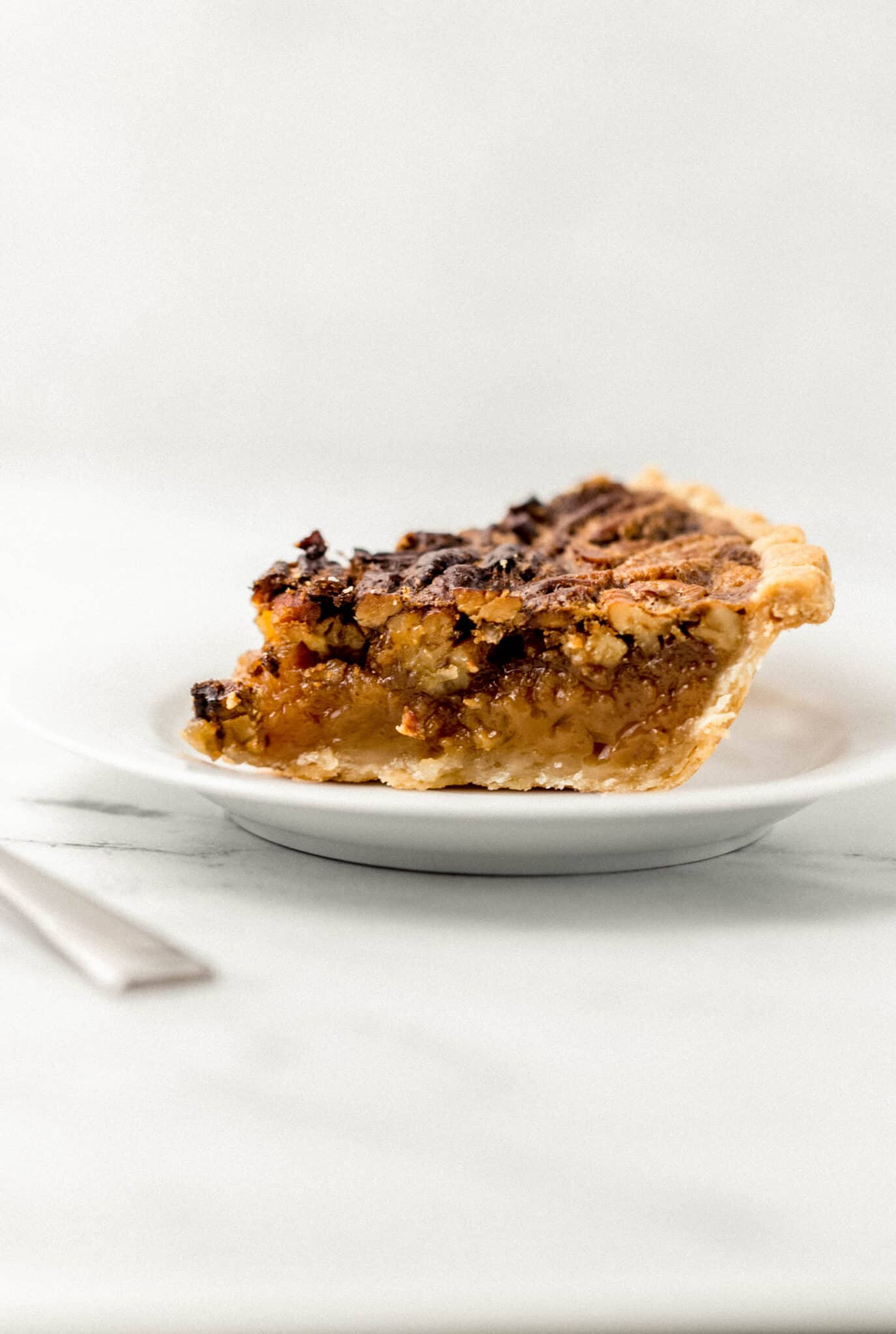 close up side view of a slice of pecan pie on a white plate 